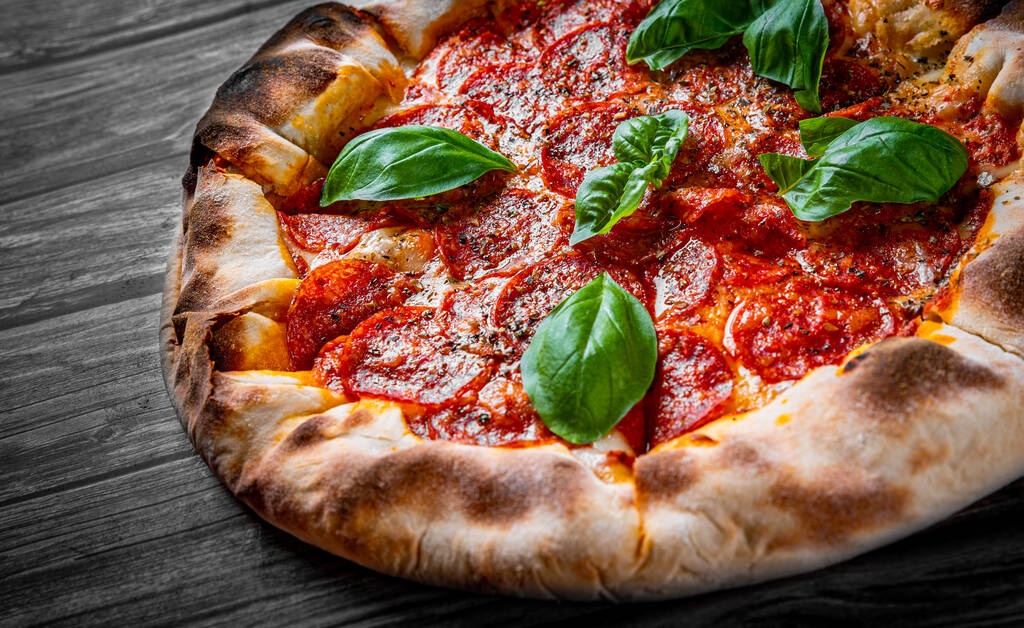 Pepperoni Pizza mit Mozzarella, Salami, Tomatensauce, Pfeffer, Gewürzen und frischem Basilikum. Italienische Pizza auf Holztischhintergrund - Foto, Bild
