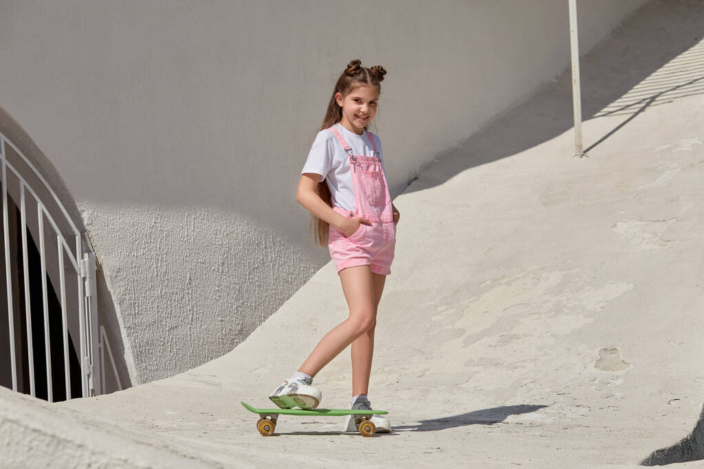 Menina fina bonita com um skate no fundo de um edifício leve
. - Foto, Imagem