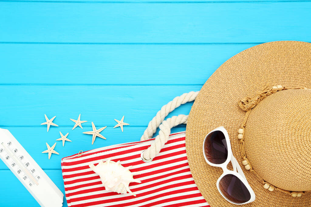 Letni słomkowy kapelusz z torebką w paski, okulary przeciwsłoneczne, termometr i muszle na niebieskim drewnianym stole - Zdjęcie, obraz