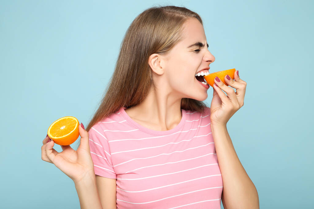 Menina comendo fruta laranja fresca no fundo azul
 - Foto, Imagem