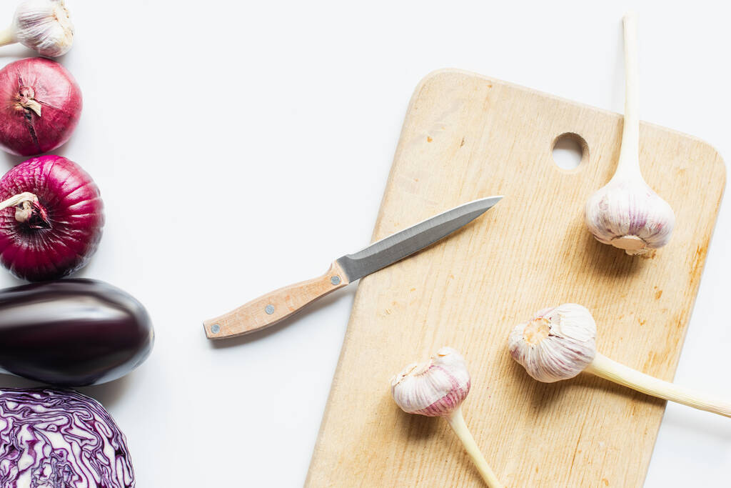 vista dall'alto di cipolla rossa, cavolo rosso, melanzane e aglio vicino tagliere in legno con coltello su sfondo bianco - Foto, immagini