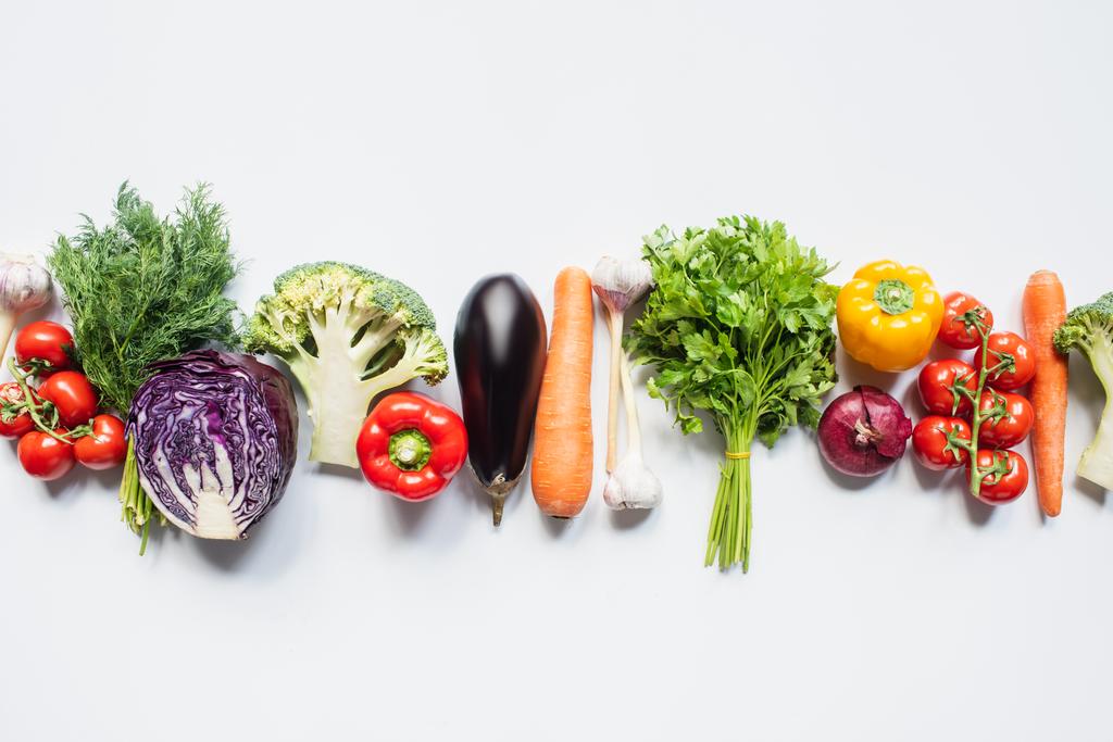 bovenaanzicht van kleurrijke geassorteerde verse groenten in lijn met witte achtergrond - Foto, afbeelding