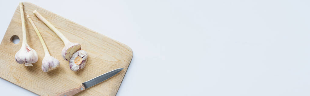 πάνω όψη του σκόρδου σε ξύλινο ξύλο κοπής σκάφους με μαχαίρι σε λευκό φόντο, πανοραμική βολή - Φωτογραφία, εικόνα