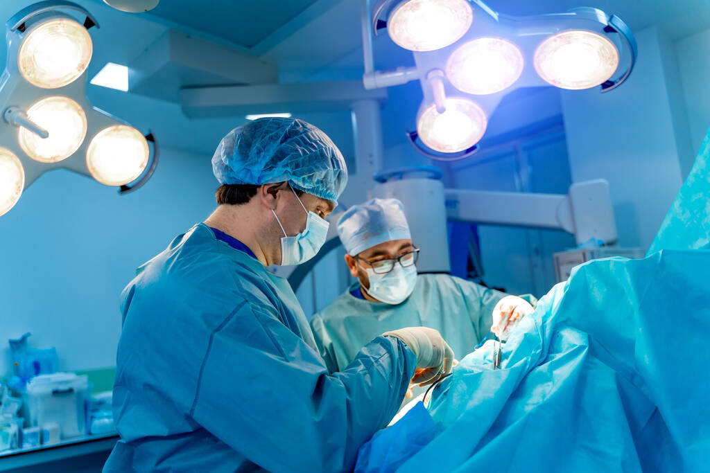Δύο λευκοί χειρουργοί κάνουν εγχείρηση. Δωμάτιο με σύγχρονο ιατρικό εξοπλισμό. - Φωτογραφία, εικόνα