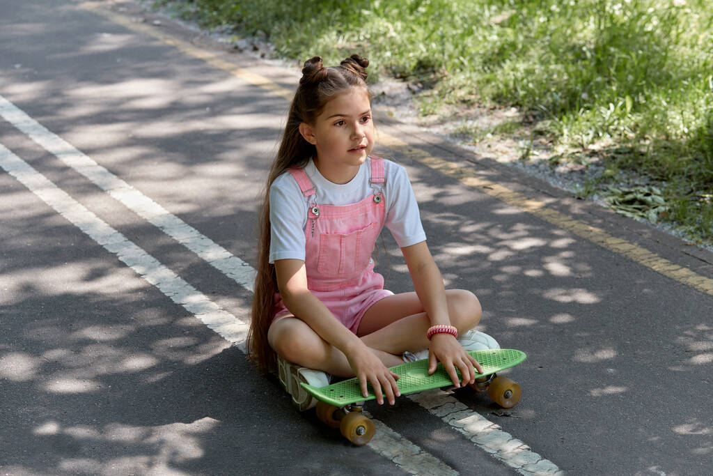 Une jolie fille mignonne est assise sur la piste avec un skateboard dans ses mains. - Photo, image