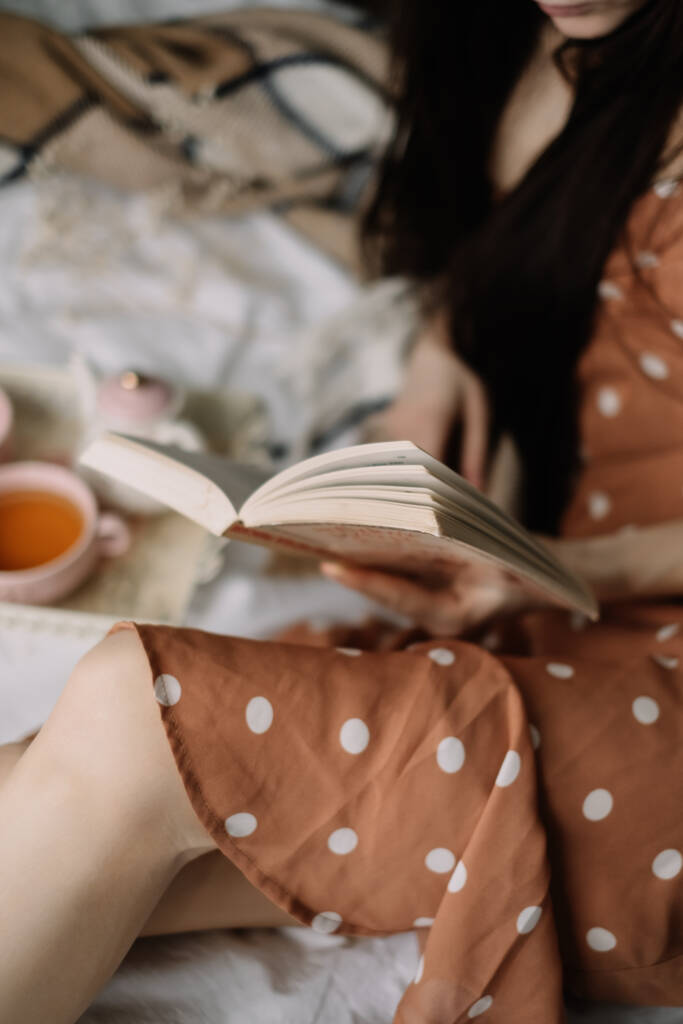 Kobieta czyta książkę w domu w łóżku i pije herbatę, wypoczynek w domu w przytulności i wygodzie. Wysokiej jakości zdjęcie - Zdjęcie, obraz
