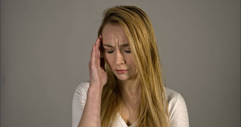 Başı ağrıyan genç bir kadın, gri arka planda soyutlanmış. - Fotoğraf, Görsel