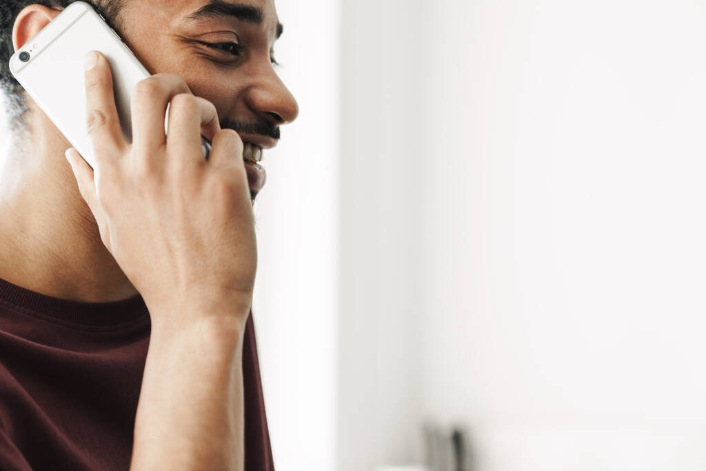 Фотознімок радісного афро - американського чоловіка, який посміхається і розмовляє по мобільному телефону вдома. - Фото, зображення