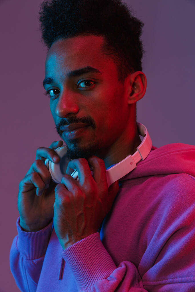 Muotokuva houkutteleva afrikkalainen amerikkalainen mies värikäs huppari poseeraa kuulokkeet eristetty violetti tausta - Valokuva, kuva