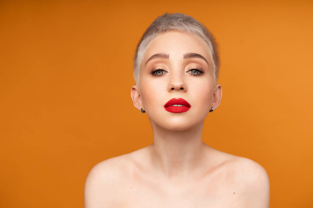 Close up fashion portrait woman with short hair red lips and naked shoulders on the colored orange background. - Photo, Image