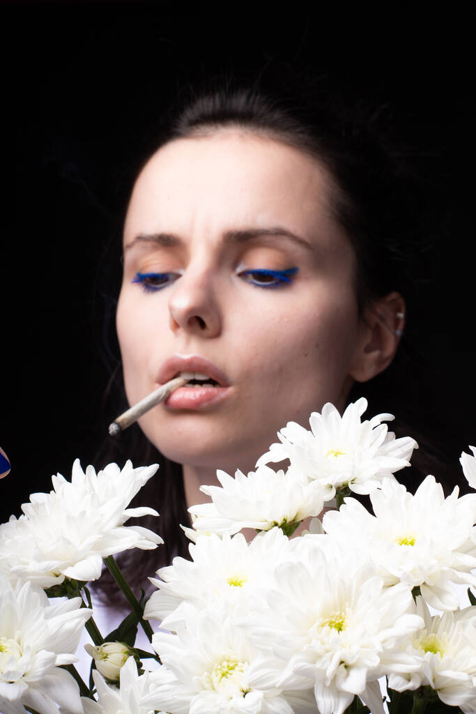 жінка з букетом білих квітів курить сигарету, чорний студійний фон
 - Фото, зображення