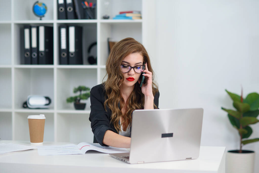 Dość stylowa kobieta biznesu w okularach prowadzenia rozmowy telefonicznej biznesu w biurze. - Zdjęcie, obraz