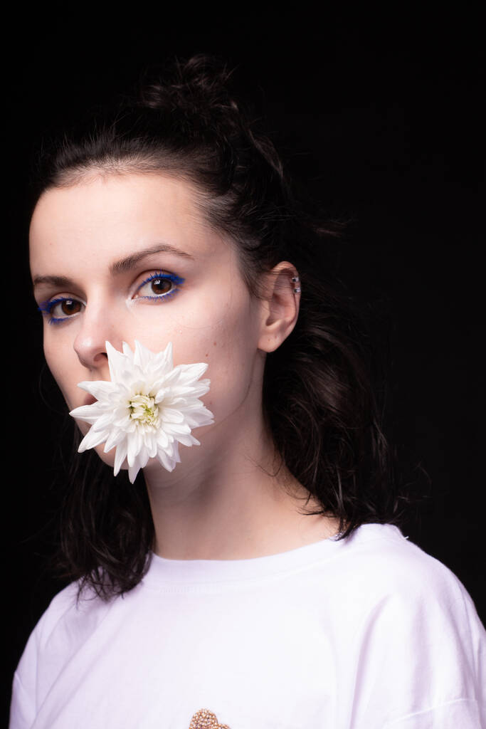 Девушка держит белый хризантем во рту, черный фон - Фото, изображение
