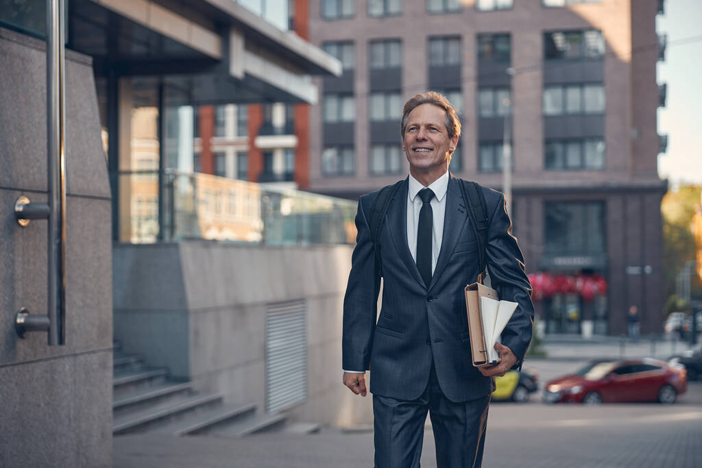 Vrolijke zakenman met papieren die op straat lopen - Foto, afbeelding