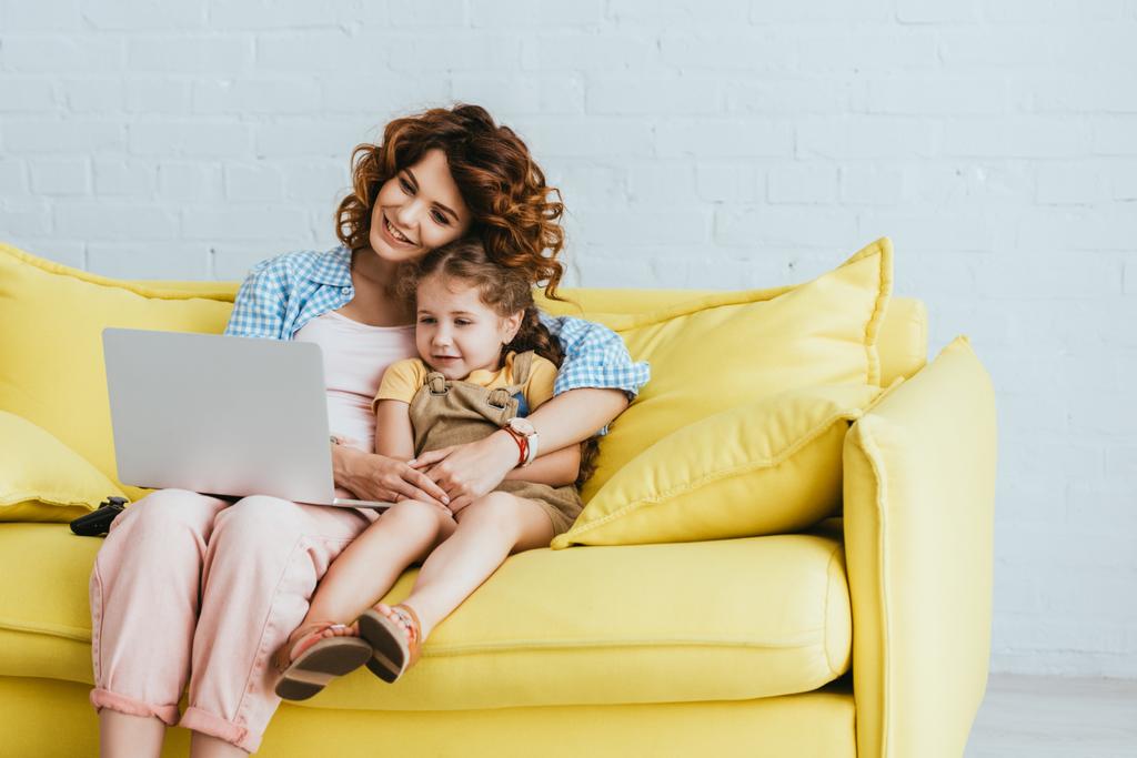 babá sorridente e criança sentados no sofá e usando laptop juntos
 - Foto, Imagem