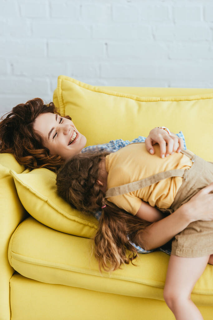 dítě ležící na smích chůva, zatímco se baví na pohovce doma - Fotografie, Obrázek