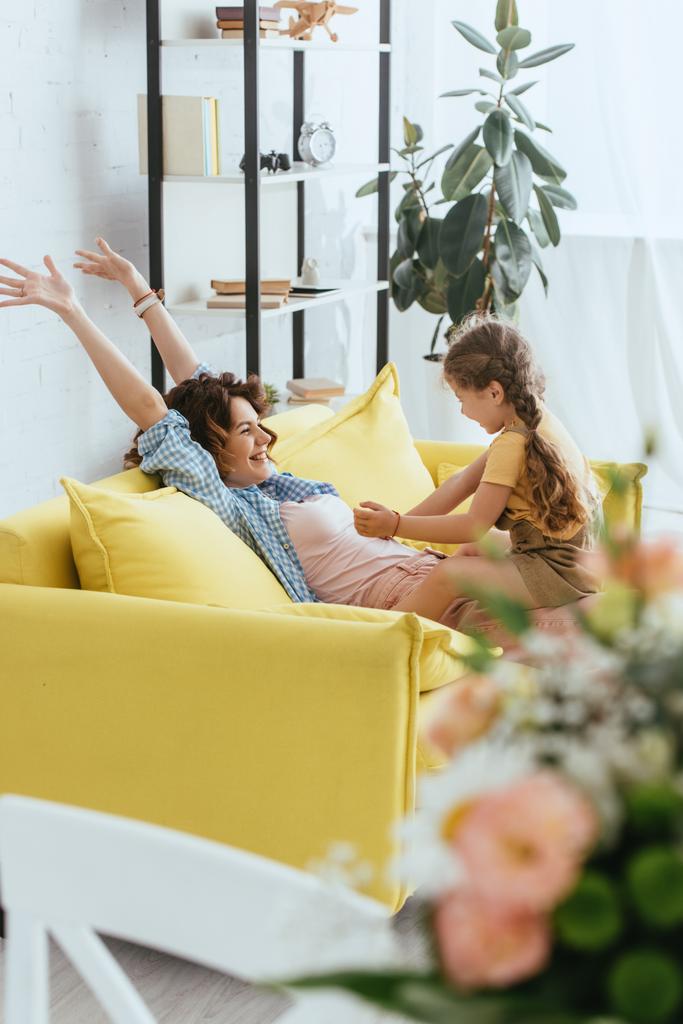 enfoque selectivo de niño cosquillas riéndose niñera mientras se divierten en el sofá - Foto, Imagen