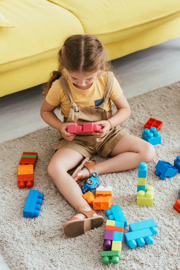 высокий угол зрения ребенка, сидящего на полу и играющего с разноцветными строительными блоками - Фото, изображение