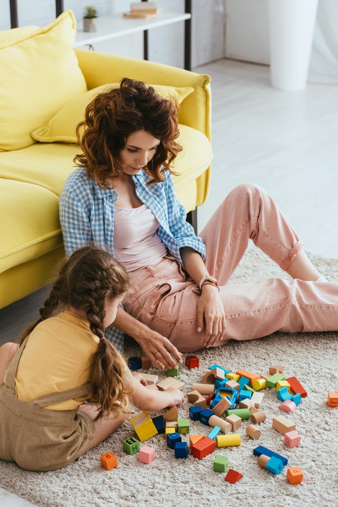 young babysitter and kid playing with multicolored blocks on floor in living room - Photo, Image