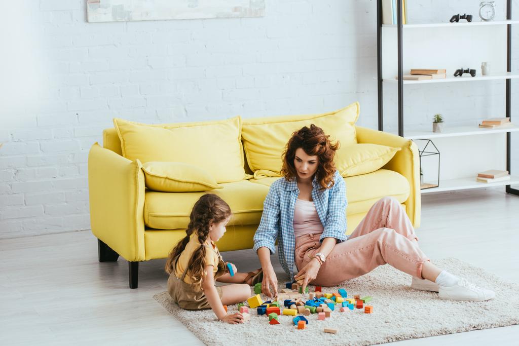 bela babá e bonito criança brincando com blocos multicoloridos no chão na sala de estar
 - Foto, Imagem