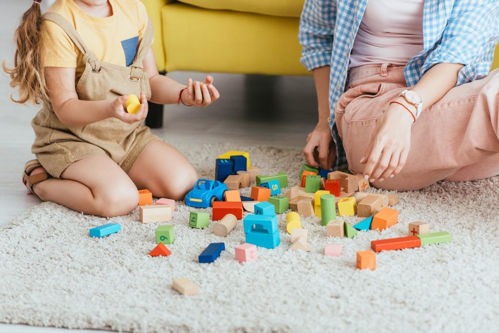 vista recortada del niño sosteniendo bloques multicolores cerca de la niñera mientras juega en el suelo - Foto, imagen