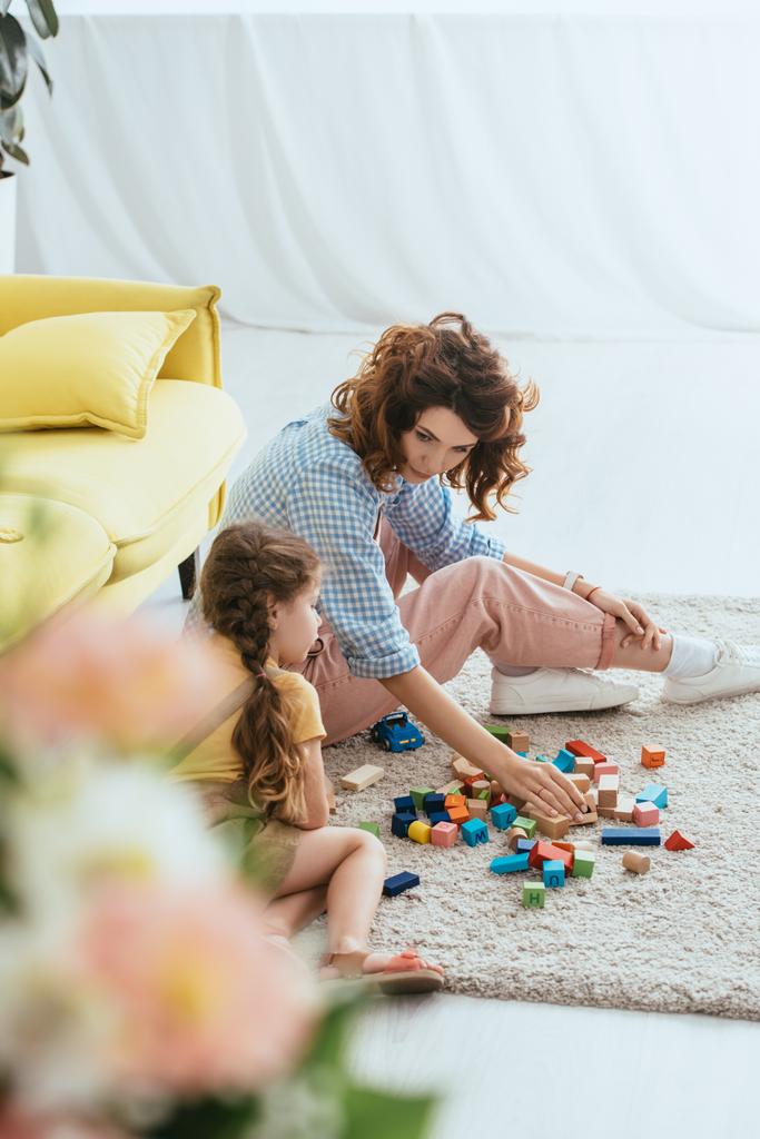 foyer sélectif de la jeune baby-sitter et enfant jouer avec des blocs multicolores sur le sol - Photo, image