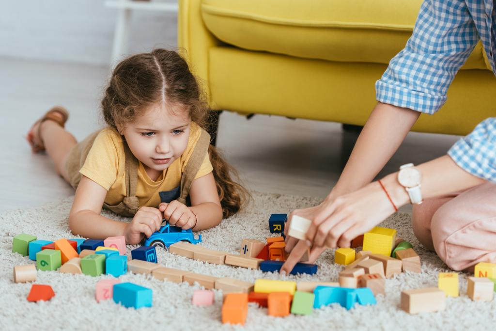 vista parcial de niñera y niño jugando con bloques multicolores de piso - Foto, imagen