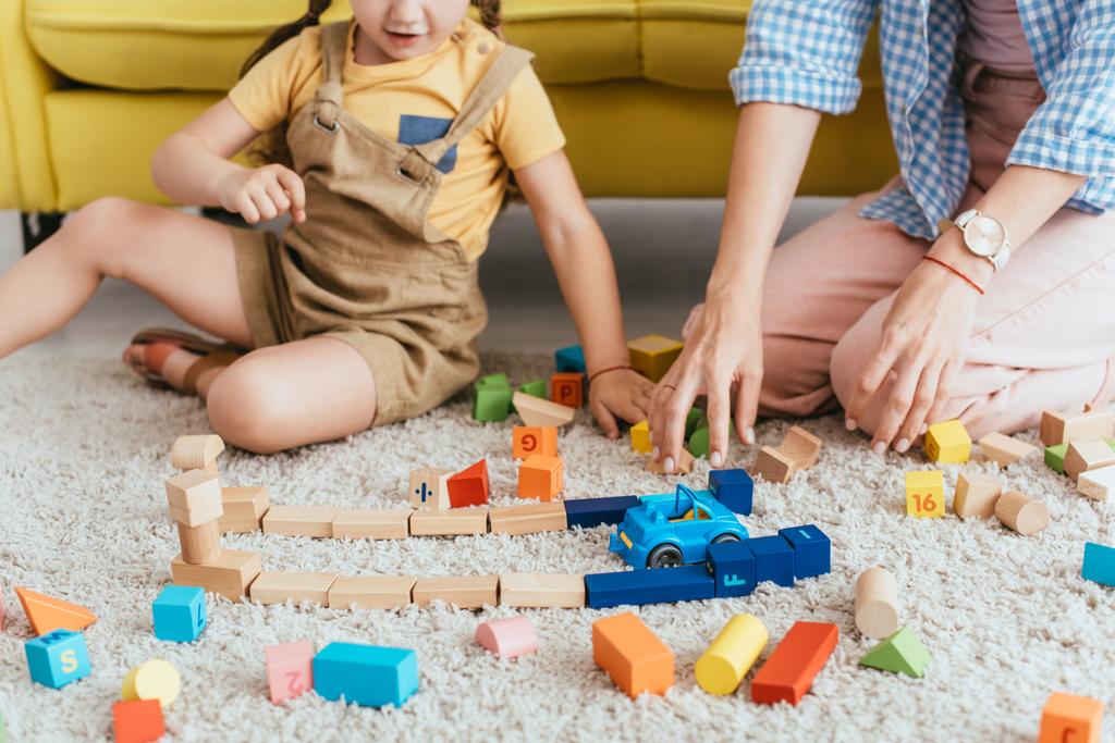 vue partielle de l'enfant et de l'infirmière jouant avec des blocs multicolores et une voiture jouet sur le sol - Photo, image