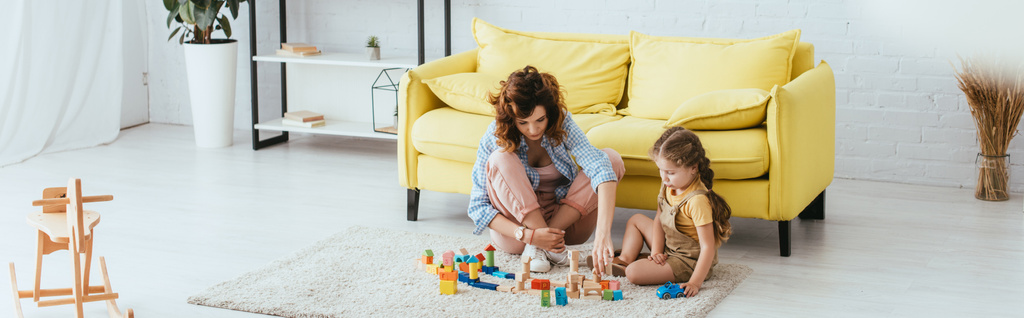 imagem horizontal de babá e criança brincando com blocos multicoloridos no chão
 - Foto, Imagem
