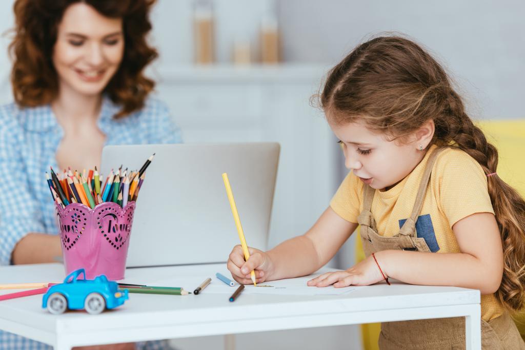 enfoque selectivo de niño lindo dibujo cerca de la niñera trabajando en el ordenador portátil - Foto, Imagen