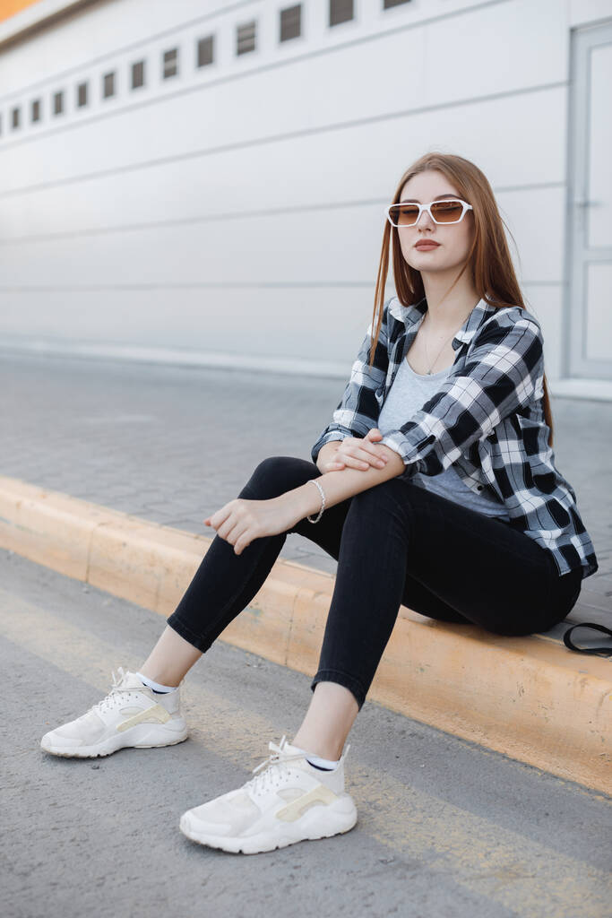 Junge Modefrau sitzt draußen vor grauem Hintergrund - Foto, Bild