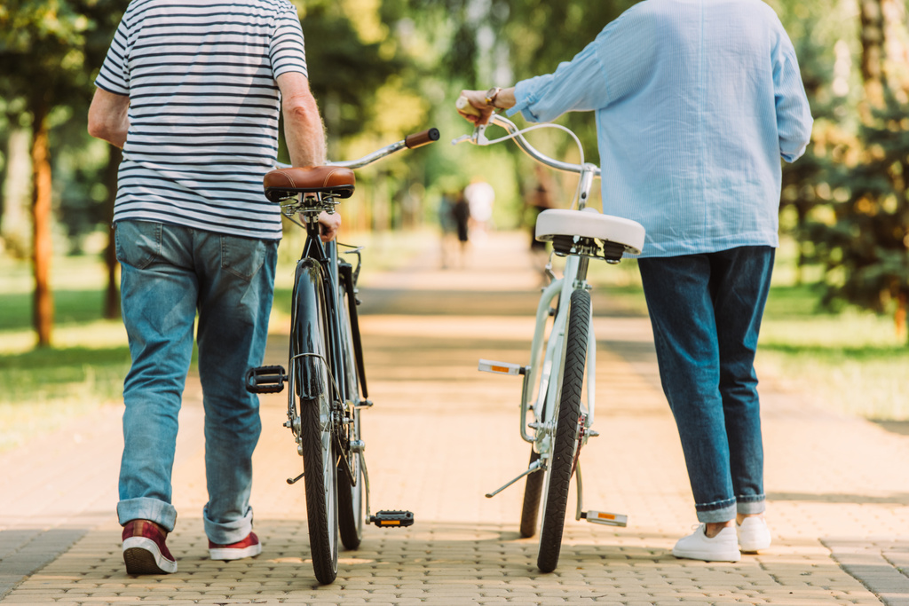 Ausgeschnittener Blick auf Senioren-Paar, das in Park in der Nähe von Fahrrädern spaziert  - Foto, Bild
