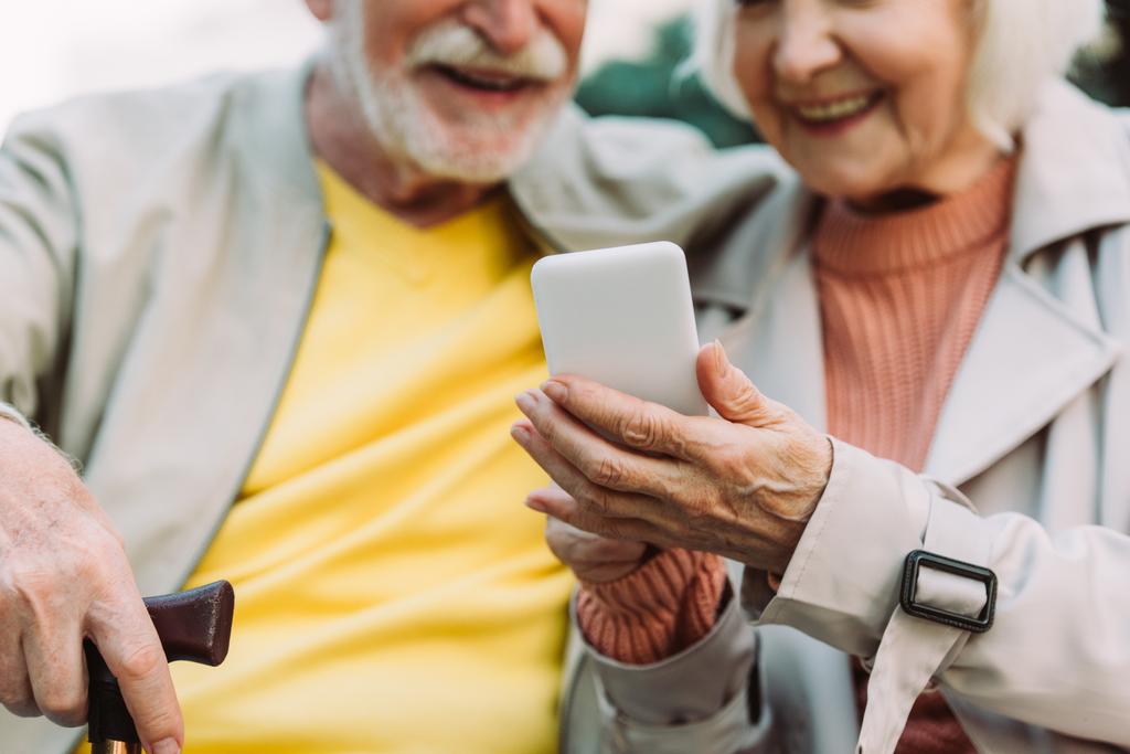 都市部の路上でスマートフォンを使用して高齢者のカップルの笑顔の作物ビュー  - 写真・画像