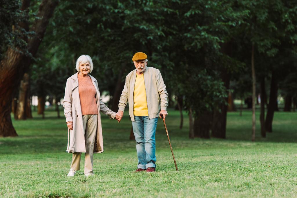 Smiling elderly woman holding hand of husband in park  - Photo, Image