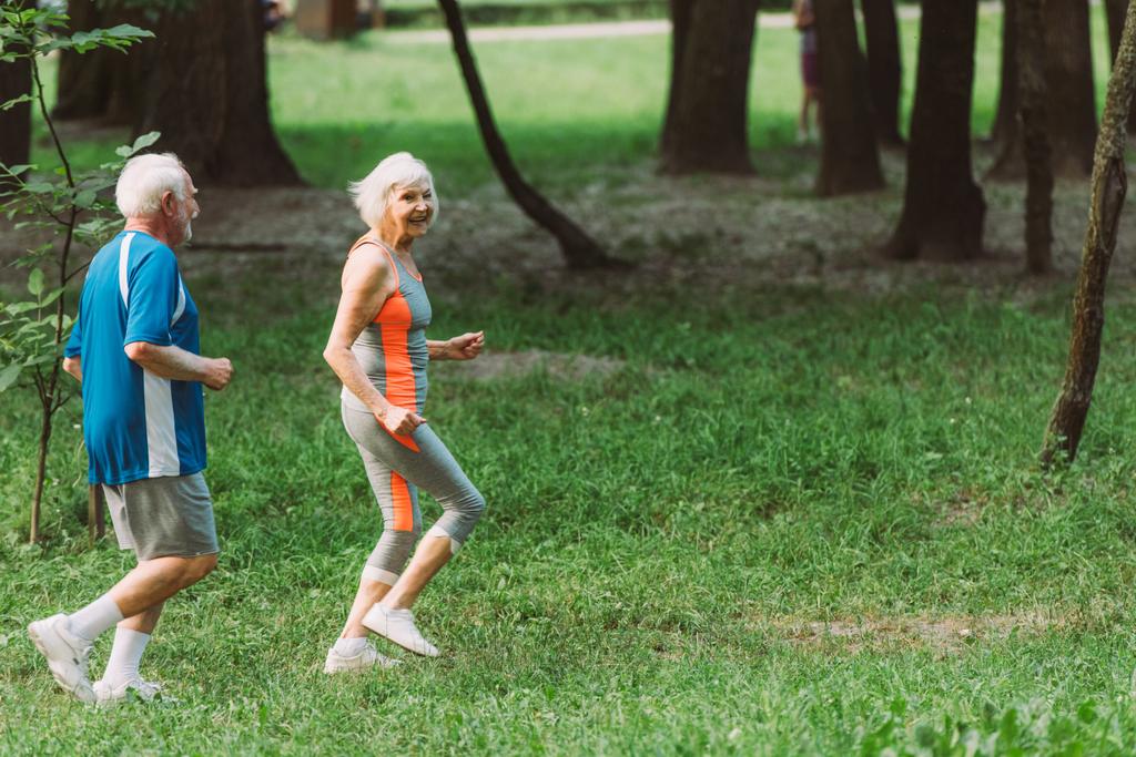 hymyilevä vanhempi nainen juoksee miehensä kanssa puistossa  - Valokuva, kuva