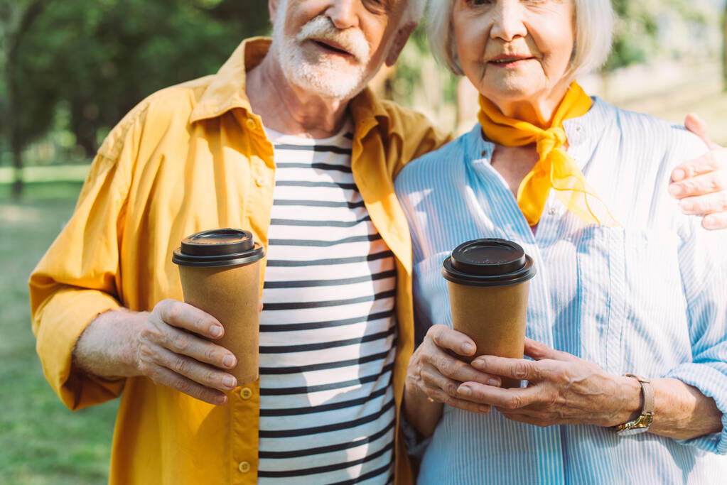 Ausgeschnittene Ansicht eines älteren Mannes, der Coffee to go hält und seine Frau im Park umarmt  - Foto, Bild