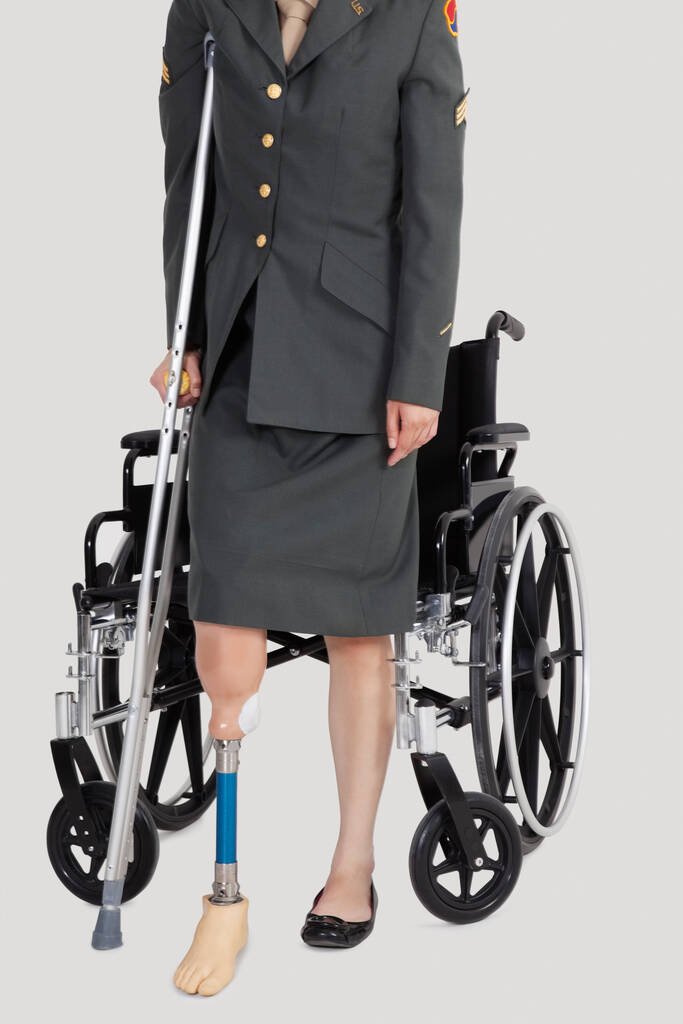 Koltuk değnekli kadın bir Amerikan subayının gri arka planda tekerlekli sandalyenin önünde durması. - Fotoğraf, Görsel