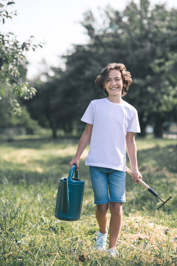 Dark-haired boy carrying the watering can and smiling - 写真・画像