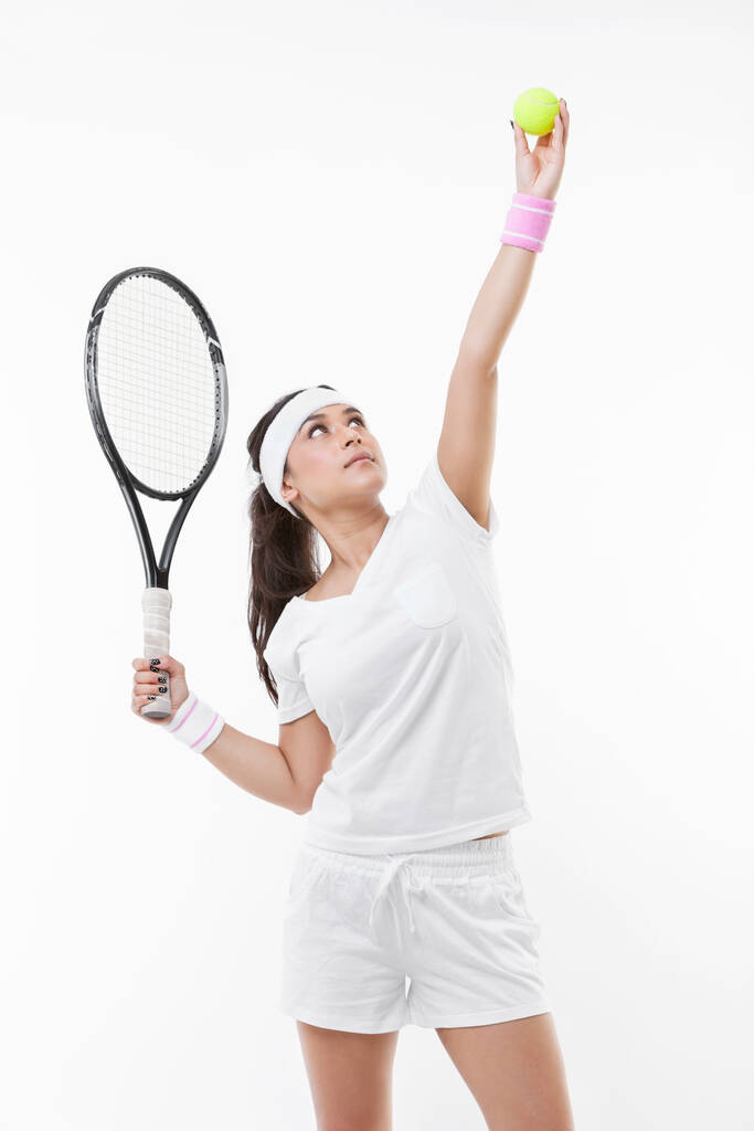 Joven jugadora de tenis preparándose para servir pelota sobre fondo blanco - Foto, imagen