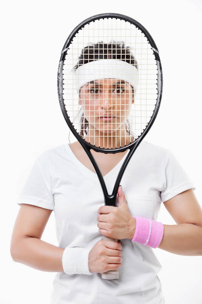 Ritratto di una giovane donna asiatica che guarda attraverso la racchetta da tennis su sfondo bianco - Foto, immagini