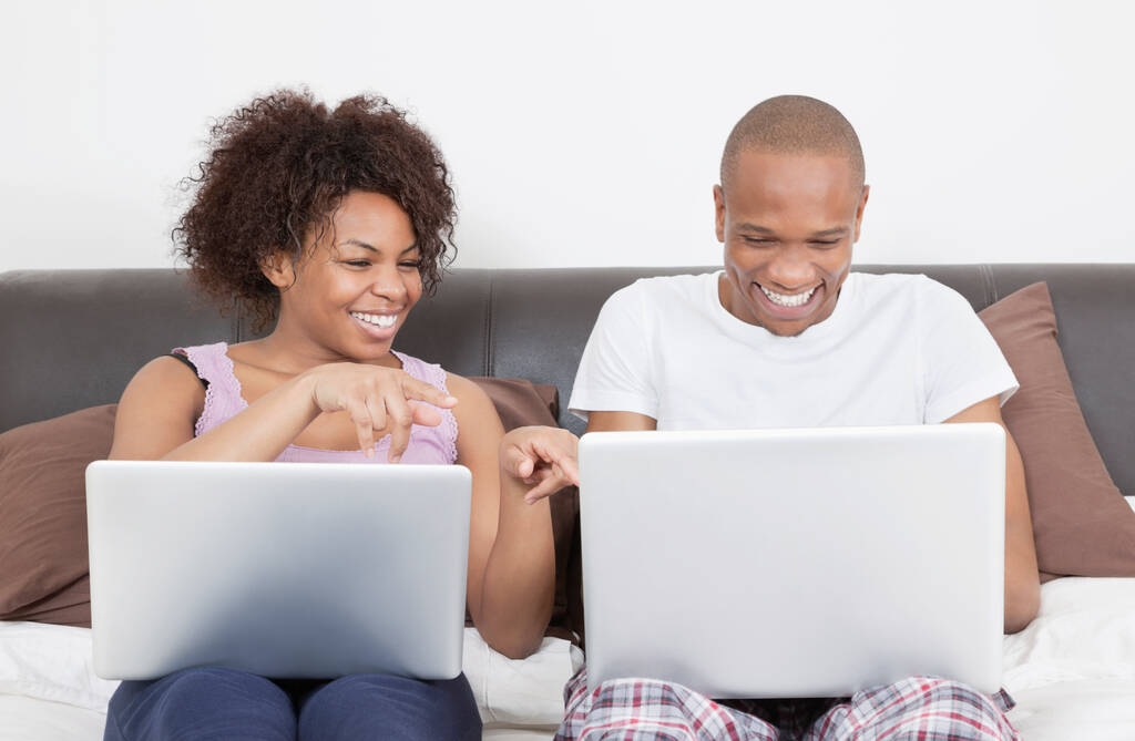 Jeune couple afro-américain excité utilisant des ordinateurs portables sur le lit - Photo, image