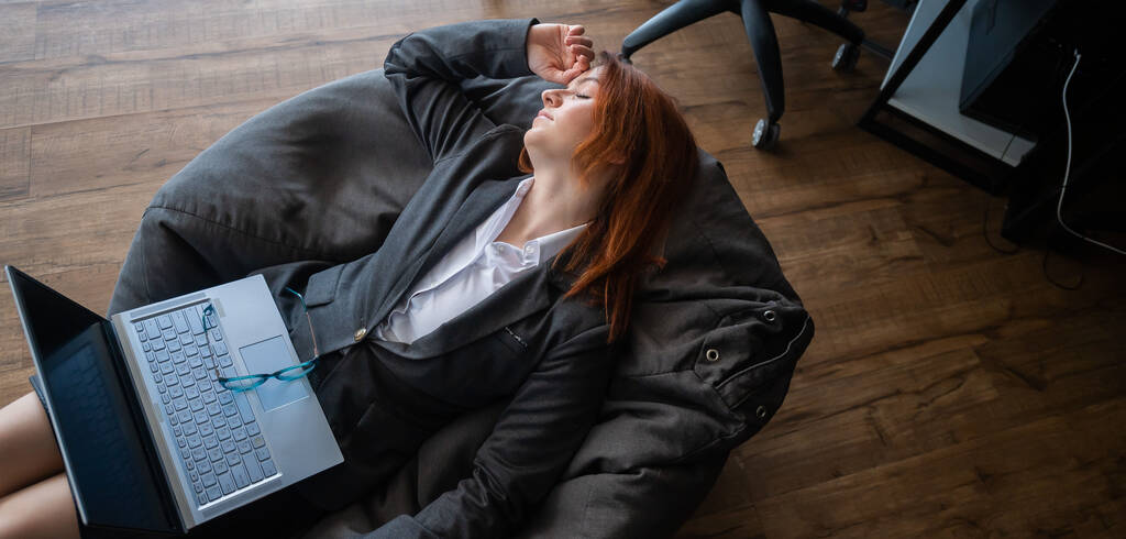 Modern iroda. Egy nő öltönyben, babzsákba bújva, laptoppal a térdén. A női menedzser egy puha székben pihen a munkahelyén. A munkavállalók kényelmének biztosítása. - Fotó, kép