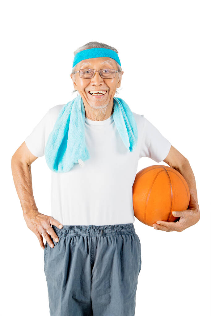 Alter Mann in Sportkleidung, während er einen Basketball in der Hand hält und im Studio steht. Isoliert auf weißem Hintergrund - Foto, Bild