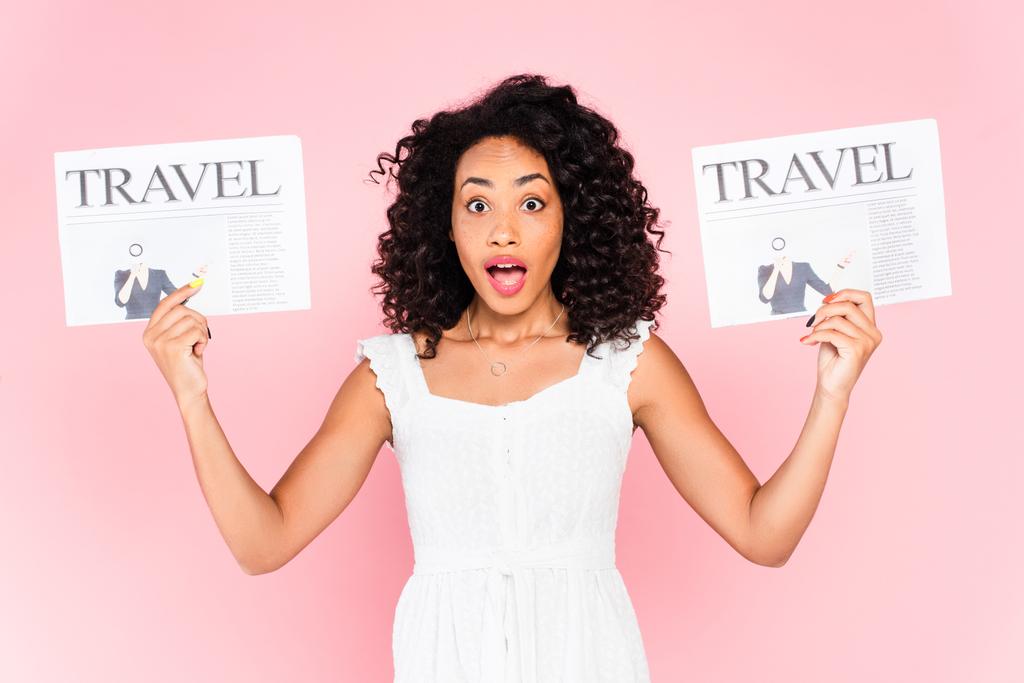 mujer afroamericana conmocionada sosteniendo periódicos de viaje aislados en rosa
  - Foto, imagen