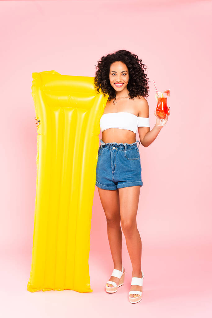 усміхнена афроамериканська дівчина тримає коктейль і надувний матрац на рожевому
  - Фото, зображення