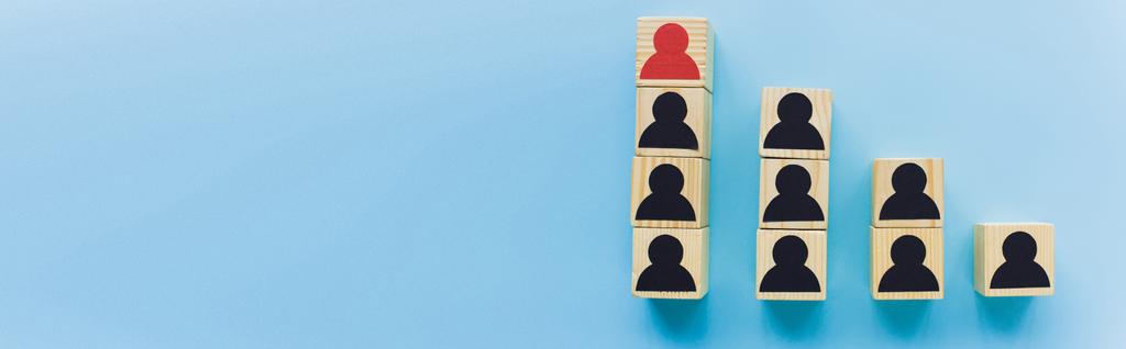 panoramisch shot van houten blokken met zwarte en rode menselijke iconen op blauwe achtergrond, leiderschap en carrière ladder concept - Foto, afbeelding
