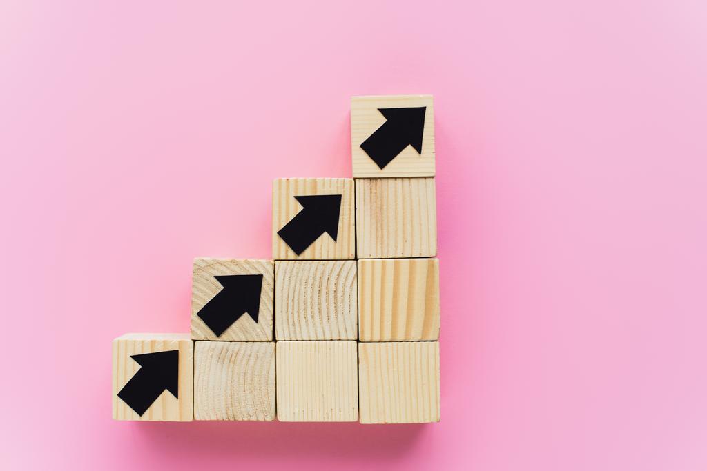 bovenaanzicht van houten blokken met zwarte pijlen op roze achtergrond, business concept  - Foto, afbeelding
