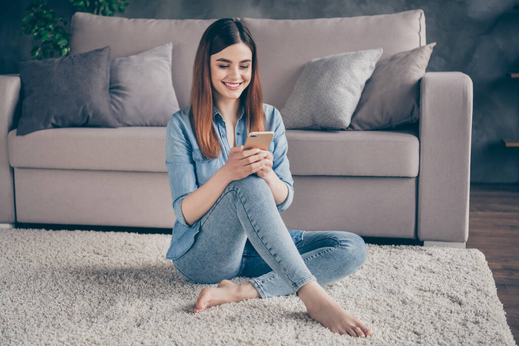 正陽気な女の子の完全な長さの写真学生座ってカーペットフロア使用スマートフォンは、屋内家の中でフォロワーとのソーシャルメディア通信を持っています - 写真・画像