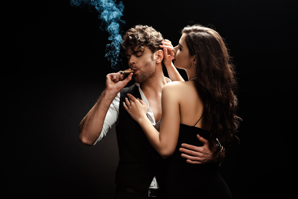 mężczyzna palenie cygaro i obejmujący dziewczyna na czarny tle - Zdjęcie, obraz