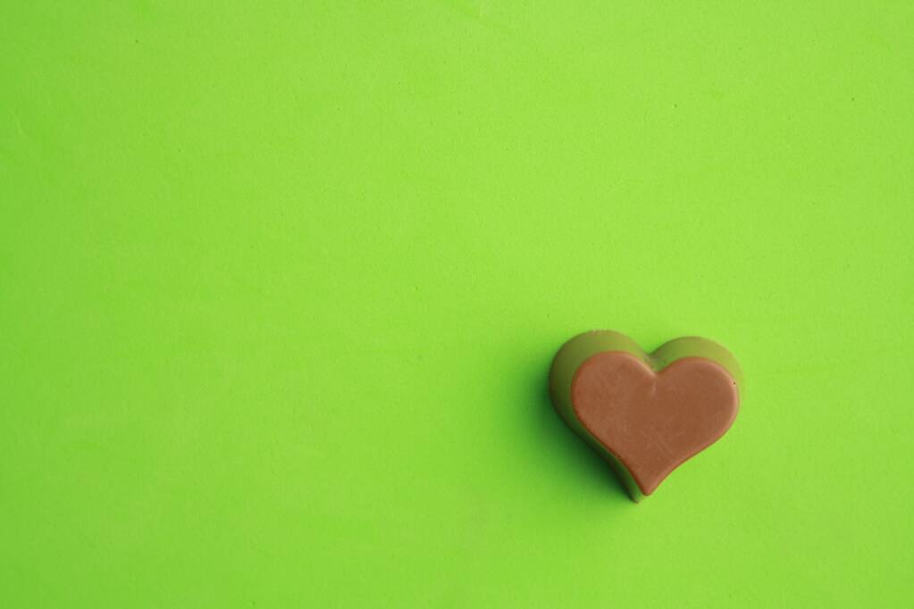 Ein Schokoladenbonbon mit Herzform auf grünem Hintergrund - Foto, Bild